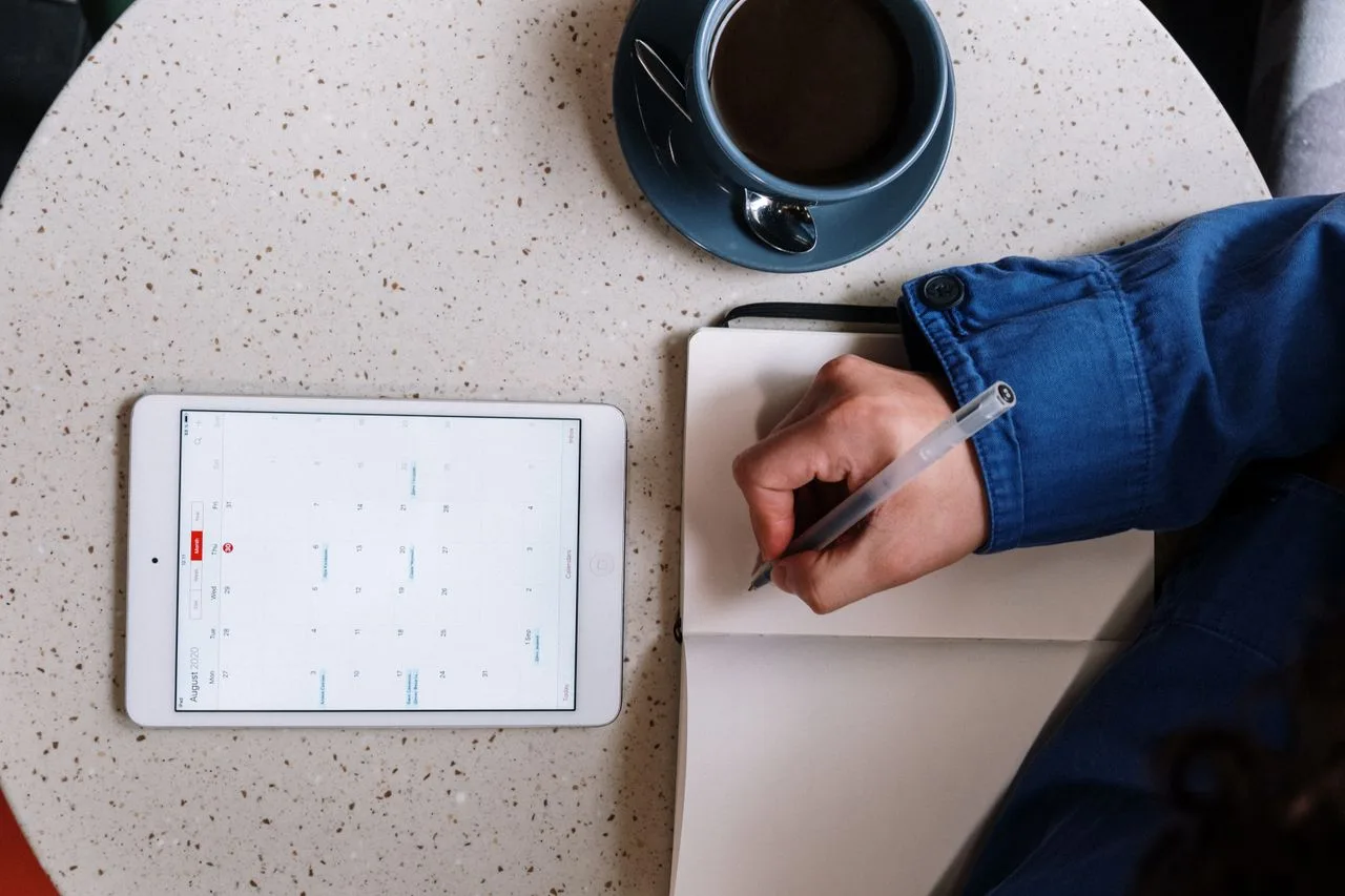 A person planning with a notebook, tablet, and cup of coffee